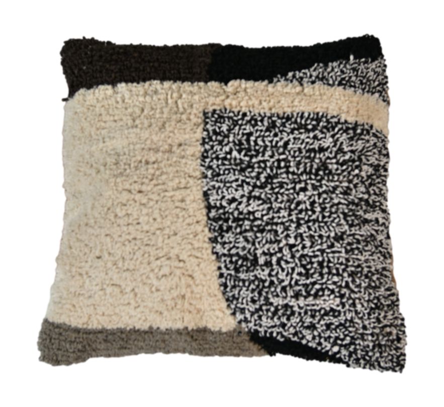 Vierkant kussen met wollige textuur in beige, zwart en bruin, met geometrisch patroon en knusse uitstraling.