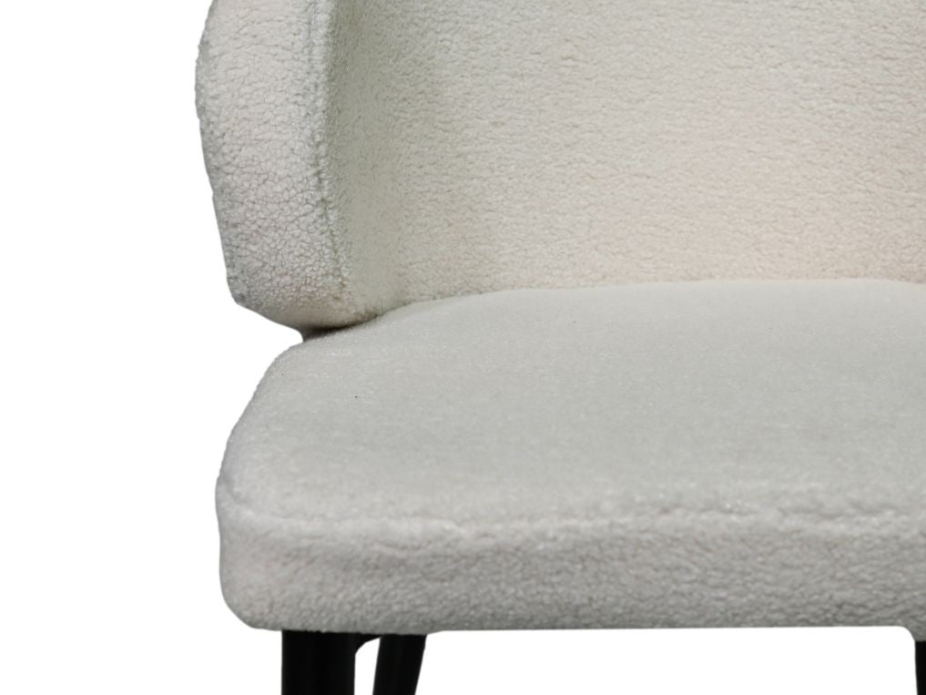 Zachte, witte stoffen stoel met moderne uitstraling en zwarte metalen poten, close-up van zitting en rugleuning.
