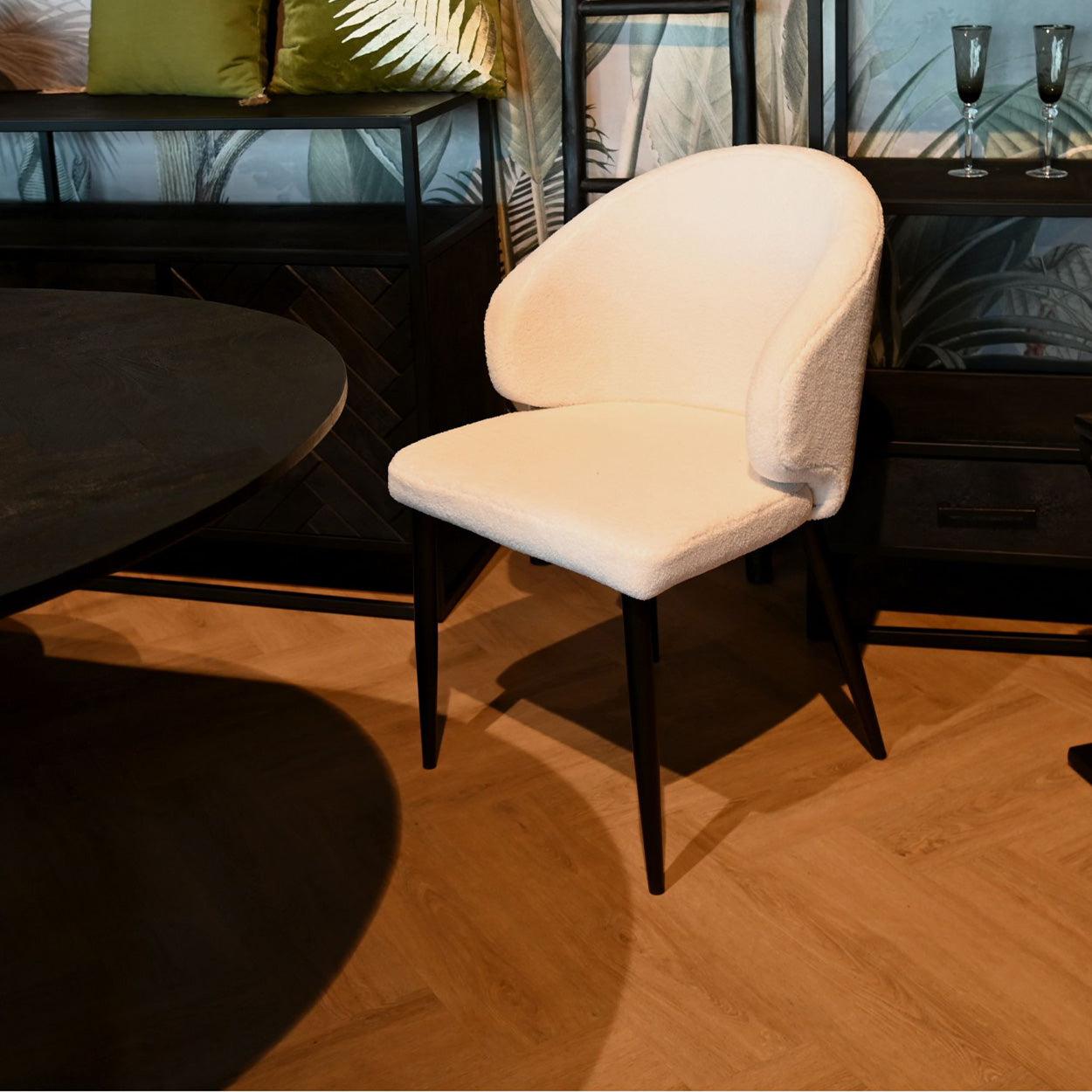 Comfortabele witte stoel met donkere poten op een houten vloer, omringd door stijlvolle meubels en decoratie.