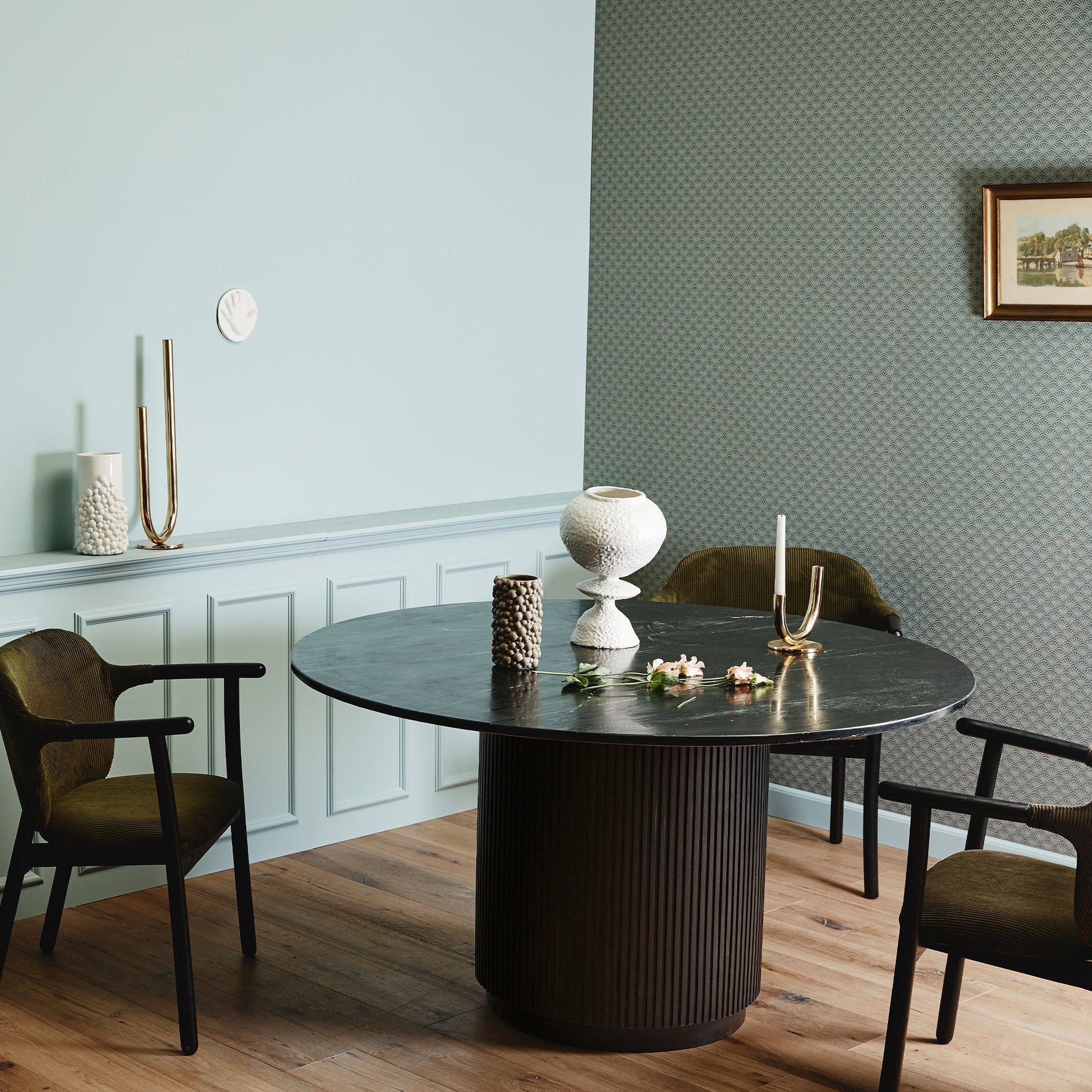 Stijlvolle eetkamer met ronde zwarte tafel, moderne decoraties, zachtblauwe muren en olijfgroene stoelen.