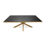 Strakke zwarte eettafel met gouden metalen frame en kruisvormige poot, minimalistisch design.
